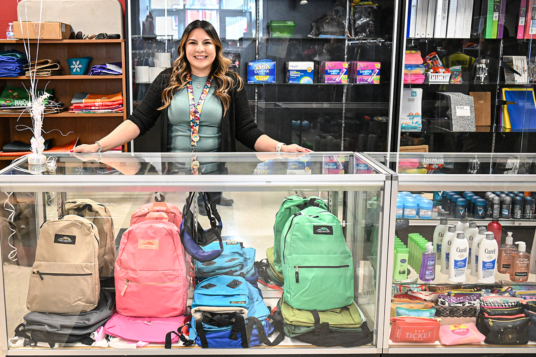 A woman smiles behind the glass case with colorful backpacks inside