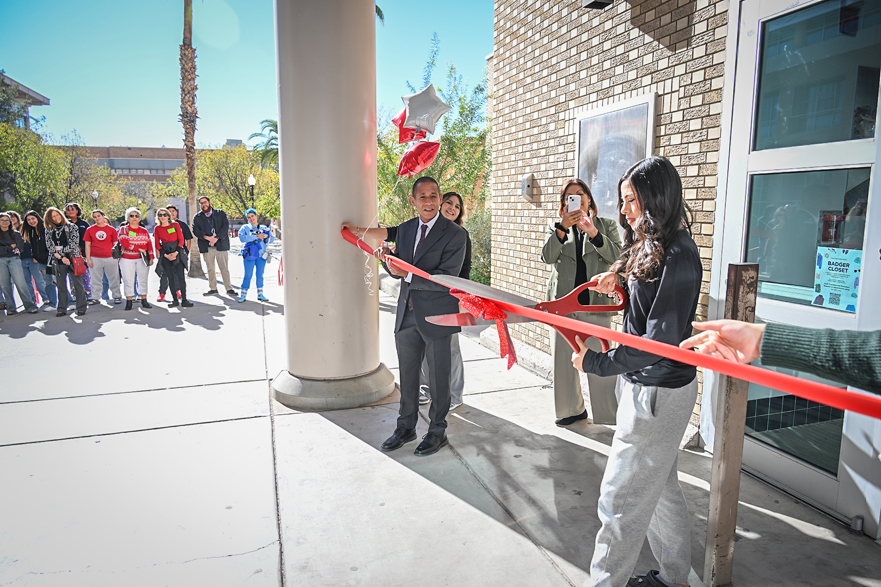 A man and woman cut a red ribbon with a pair of giant red scissors