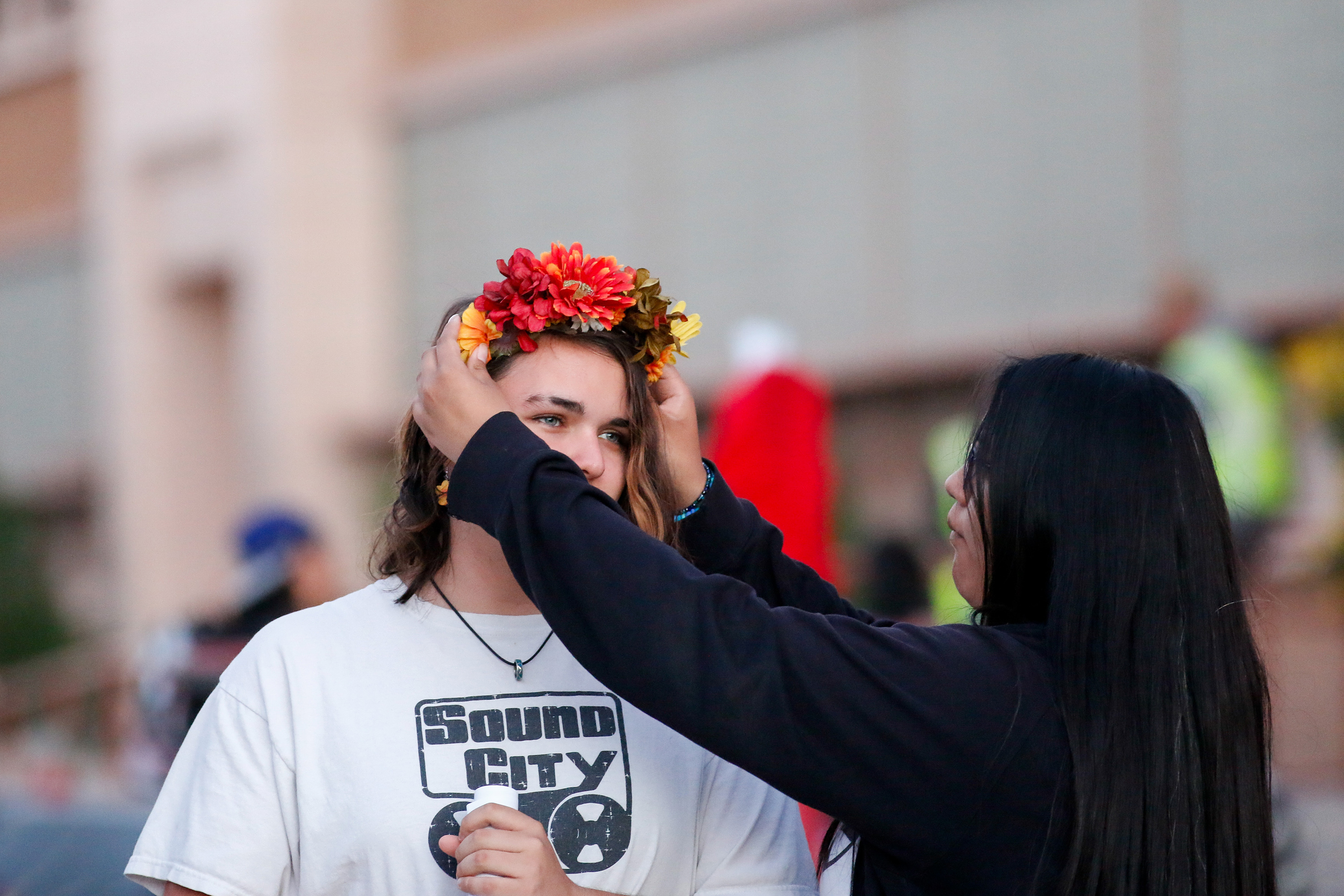 A girl in a black sweatshirt adjusts a flower crown on another girl's head