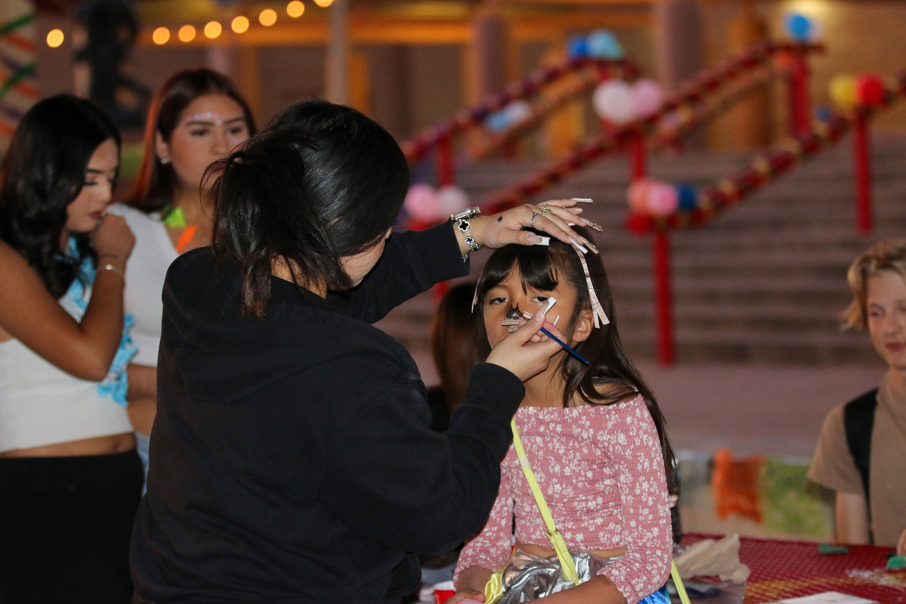 A woman in a black sweatshirt paints a little girl's face