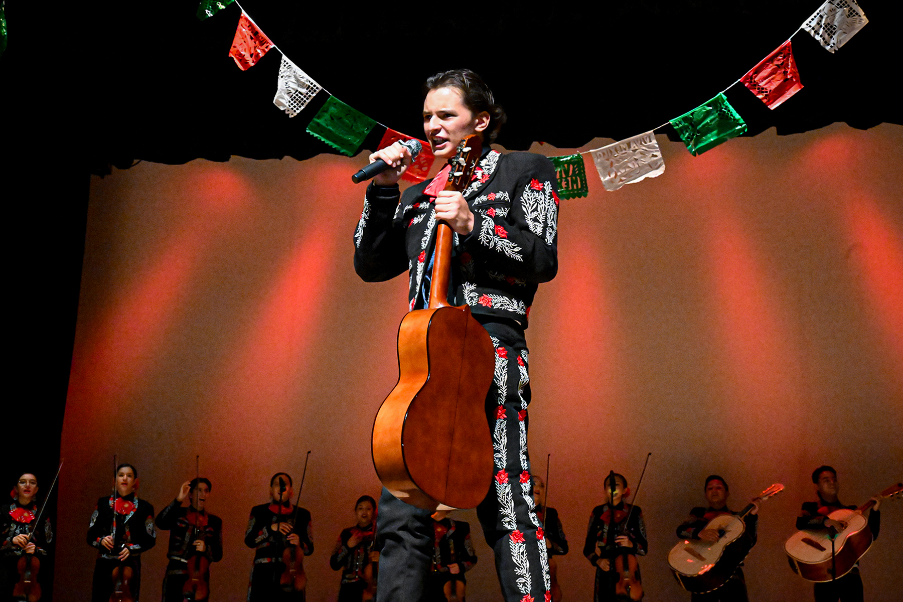 A mariachi performer holds his guitar while singing to the audience