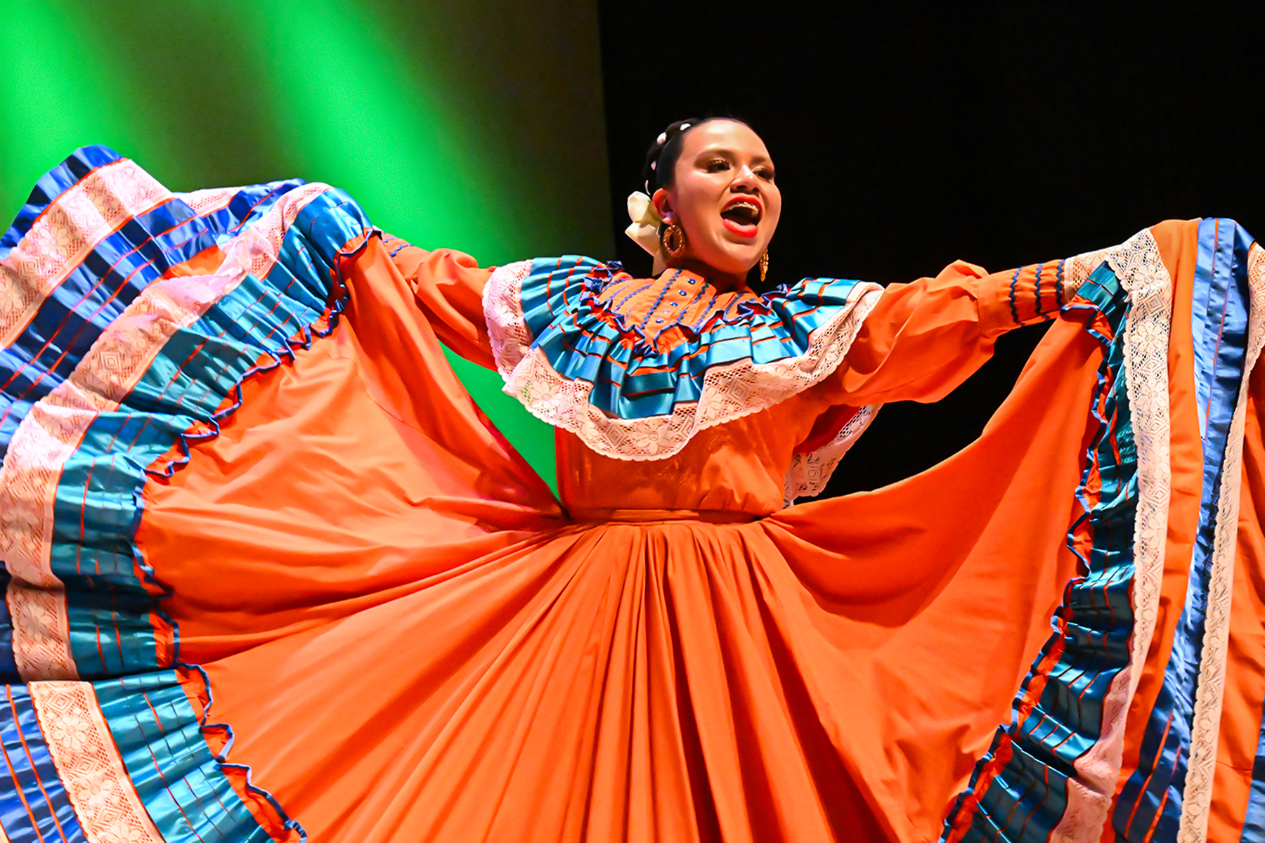 A folklorico dancer smiles in her orange dress