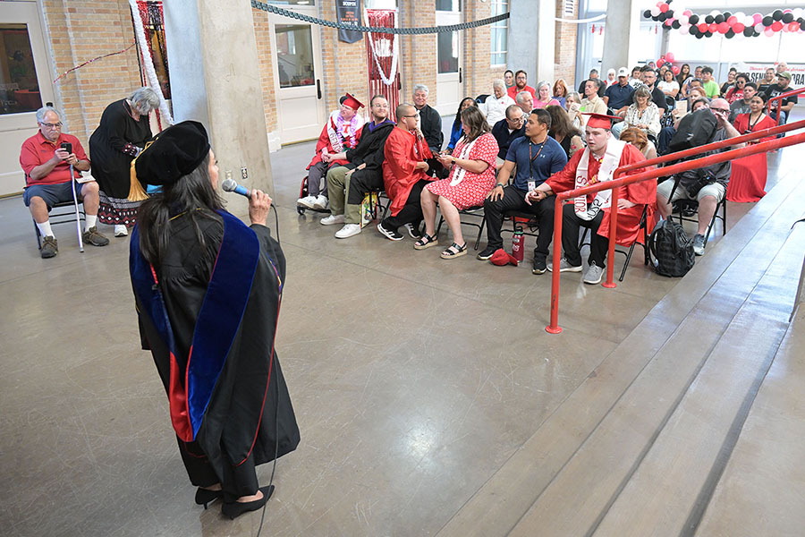 A woman in graduation regalia addresses the crowd
