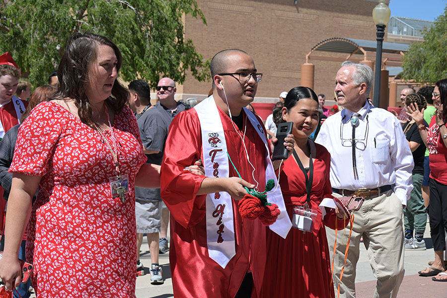 A teen boy in a red gown walks outside with his family