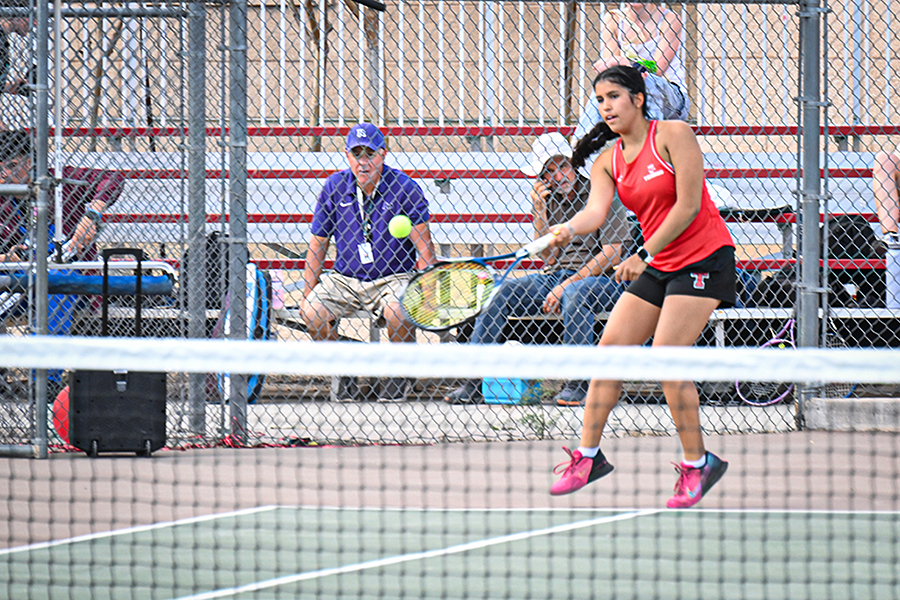 A girl holds her racquet out to hit the tennis ball back over the net