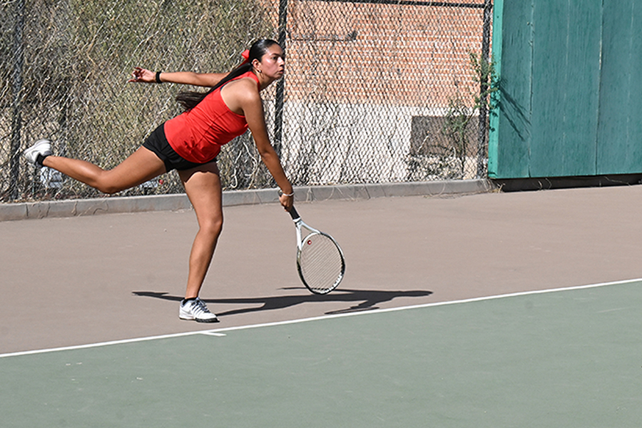 A girl stands on one leg as she swings her racquet to hit the ball