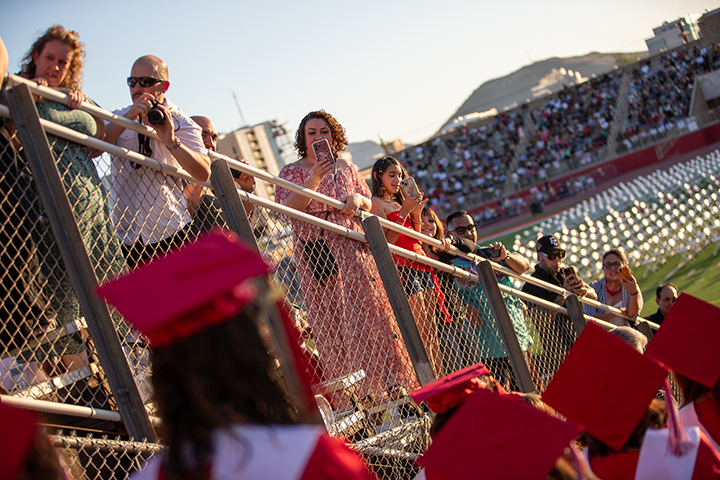 Families take photos of the graduates from the bleachers as they enter the stadium