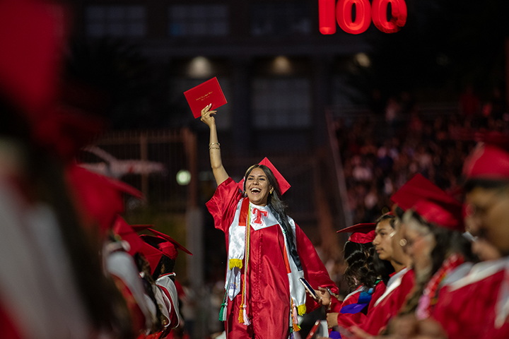 A teen girl holds up her diploma proudly