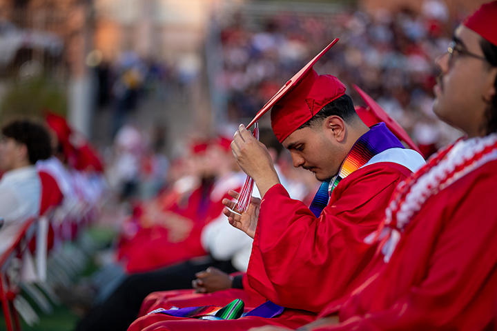 A teen boy adjusts his red grad cap