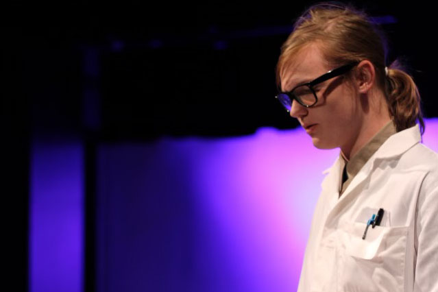 A teen boy in glasses looks down while on stage