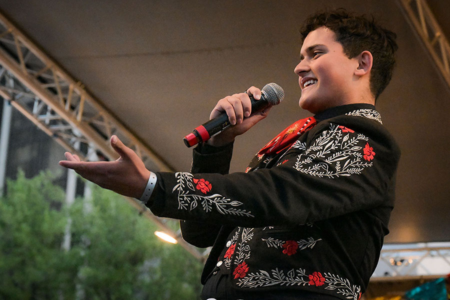 A teen boy holds out his arm as he sings into the mic