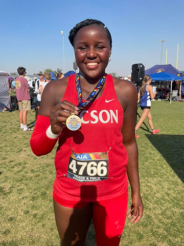 A teen girl in a red track uniform shows off her medal