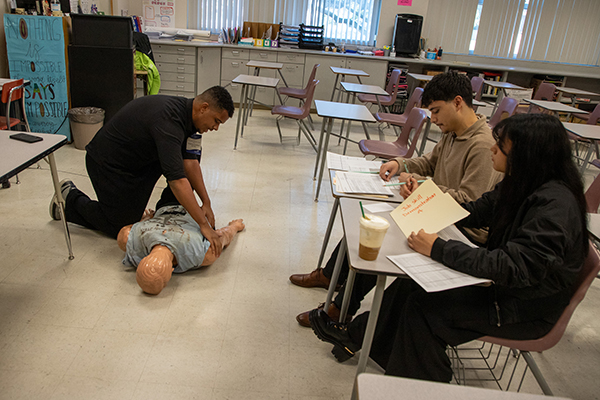 A man demonstrates CPR on a dummy to a group of students