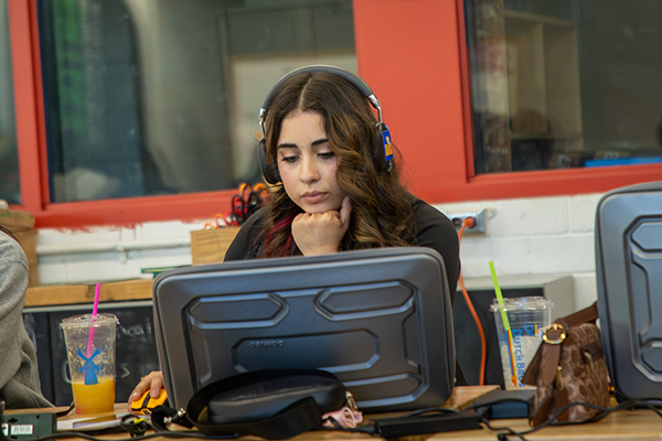 A teen girl wearing headphones works on a computer