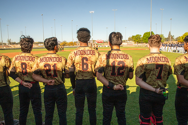 The baseball team stands facing the field for the National Anthem