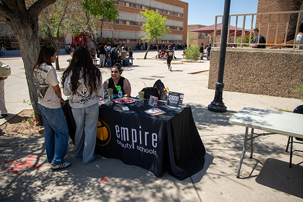 A woman from Empire Beauty Schools talks to two girls at her table