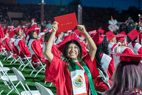 A graduate proudly holds up her diploma over her head