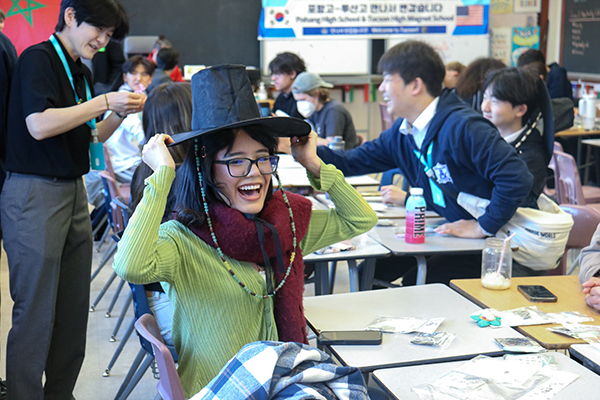 A teen girl in glasses smiles and touches her black hat
