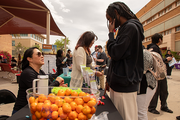 A teen boy talks to a woman sitting down at a table with a bowl of oranges