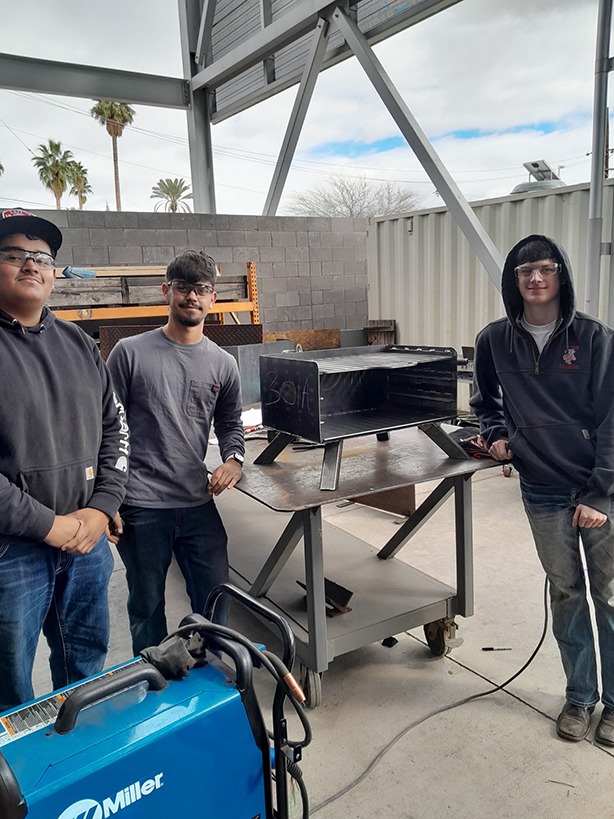 Three teen boys stand around their welding project