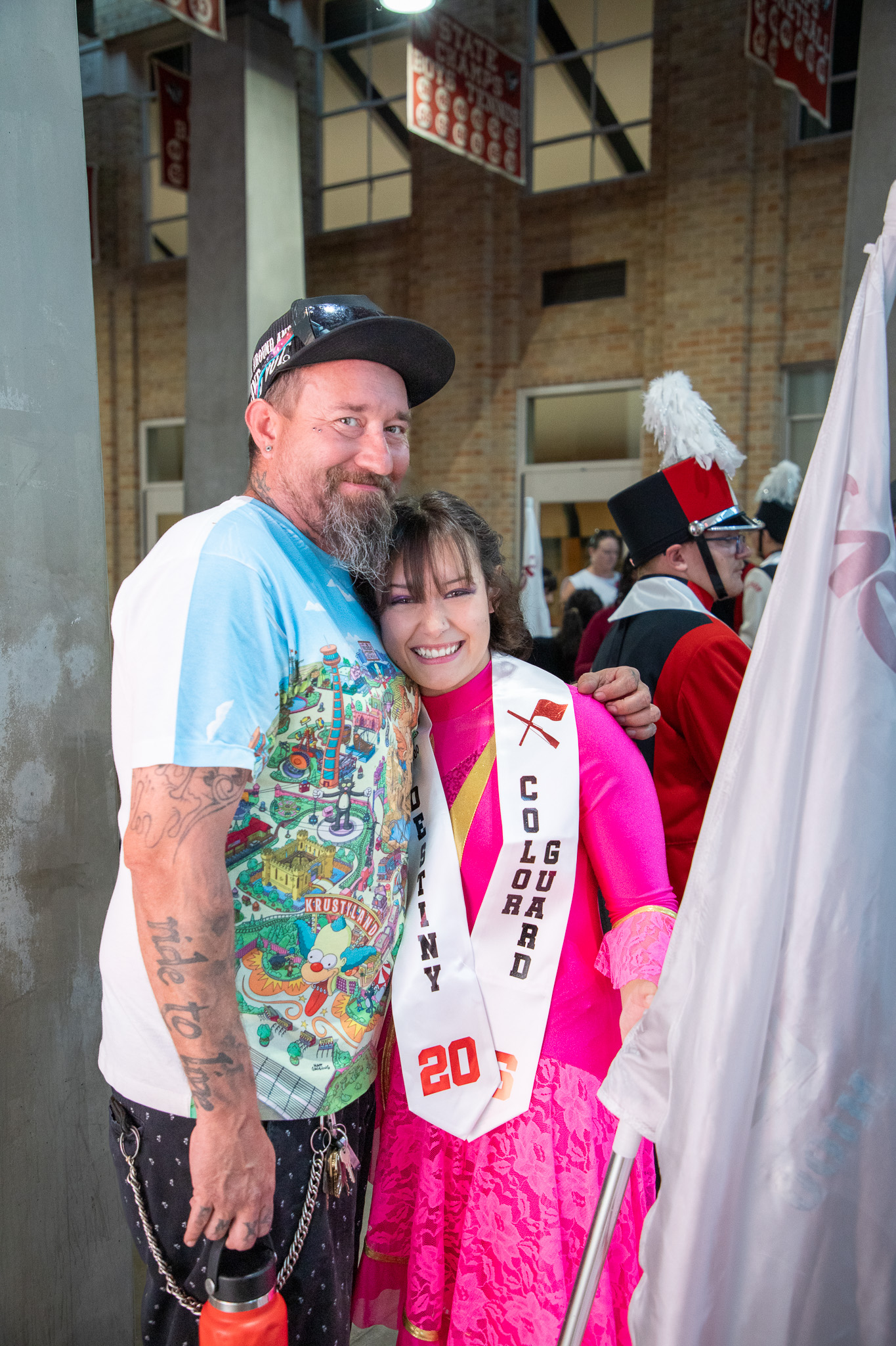 A teen girl in a color guard sash hugs her dad