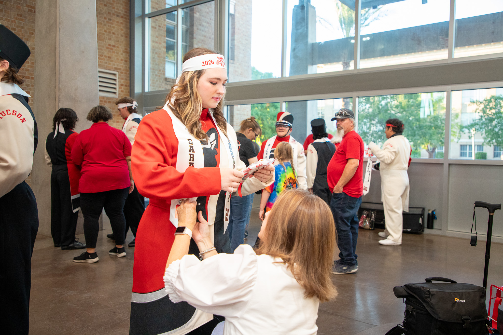 A woman kneels as she adjusts a teen girl's marching band outfit