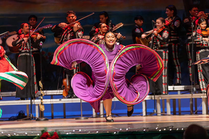 A teen girl swirls her purple dress as a mariachi performs behind her