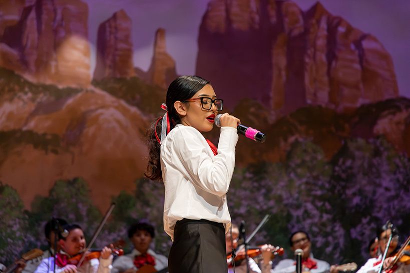A teen girl with glasses sings into a mic in front of a Sedona backdrop