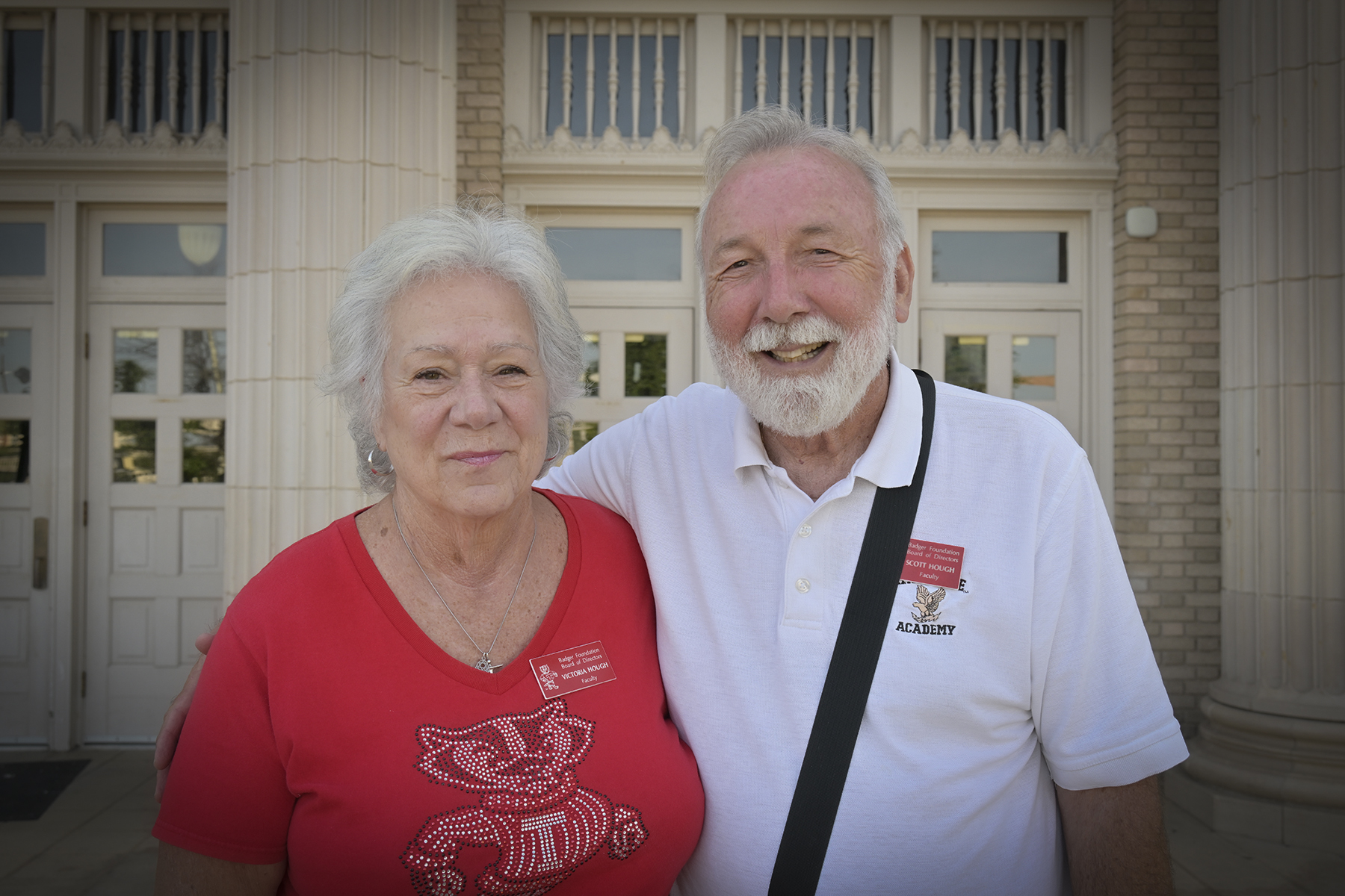 Two faculty members smile in front of the school