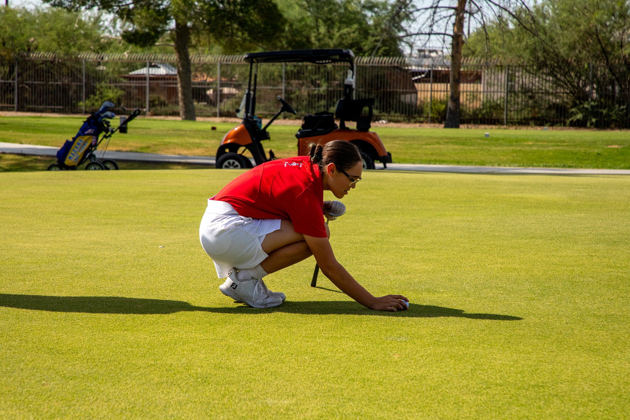 A teen girl kneels down to put her golf ball on the tee