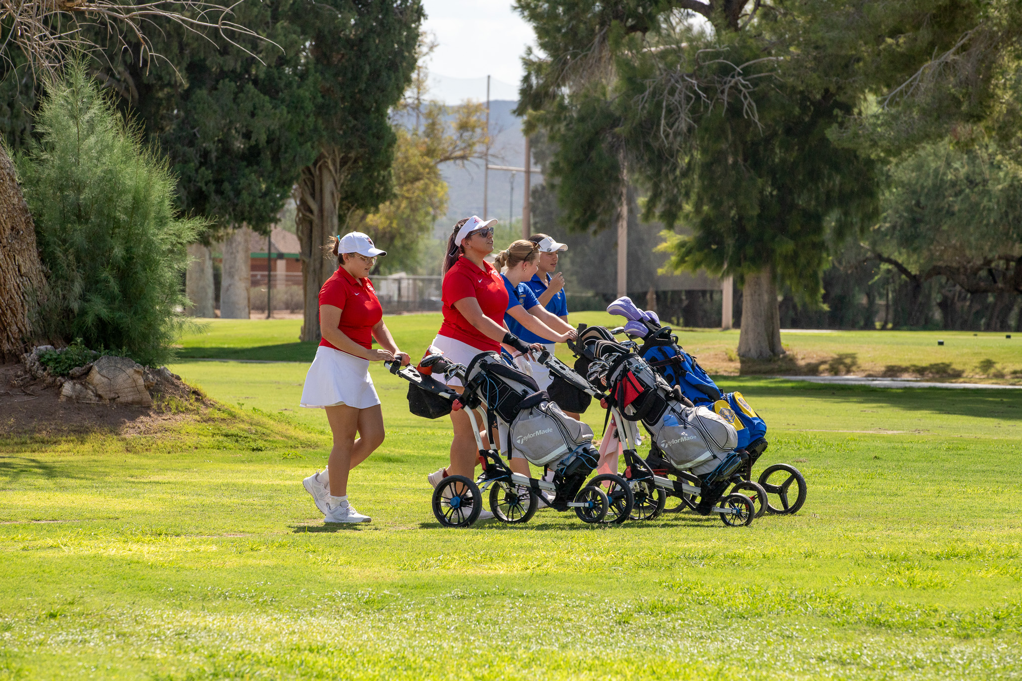 Four teen girls walk their golf caddies across the course