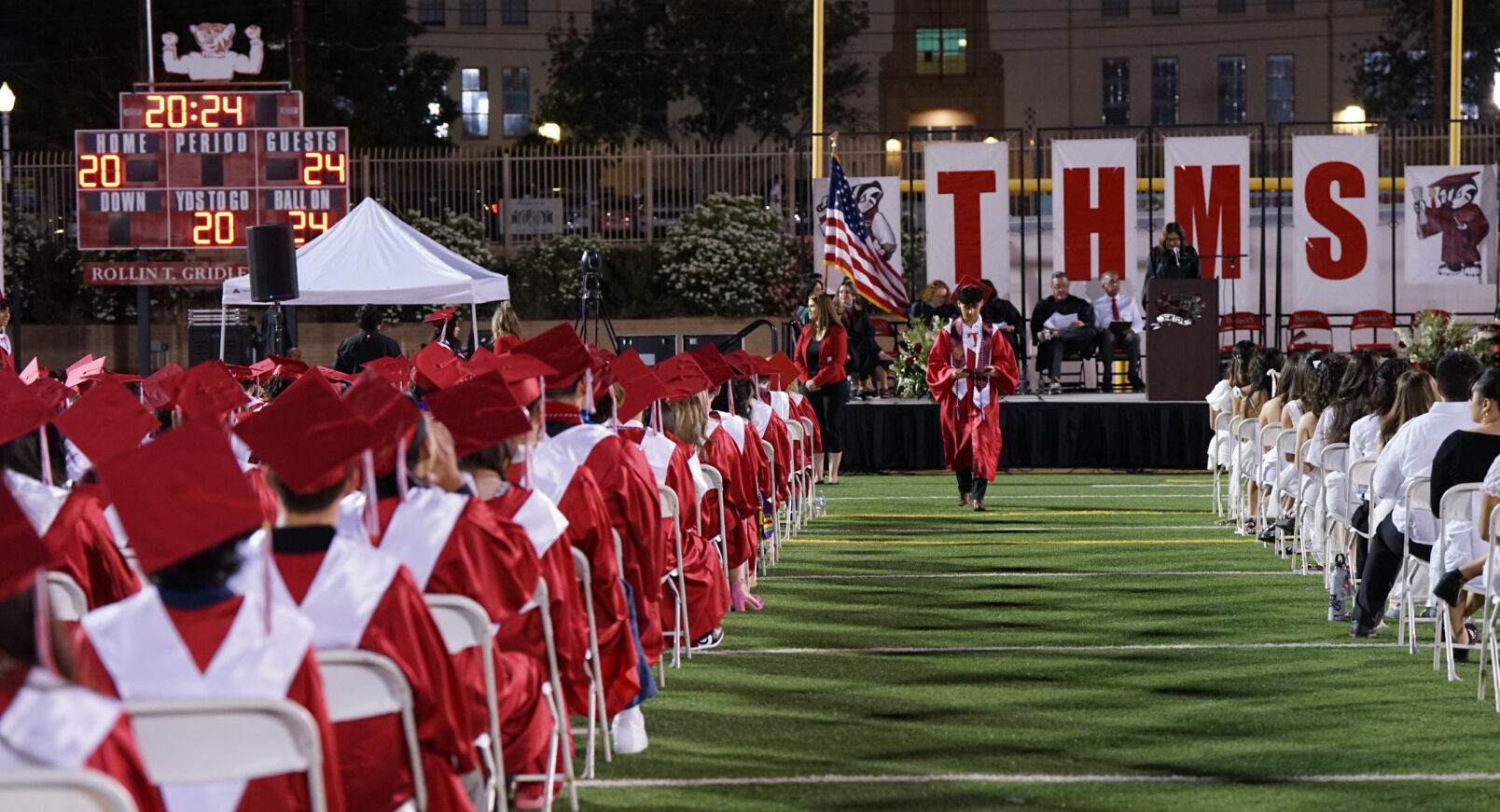 A Tucson High grad walks down the center of the field with his fellow grads seated on either side